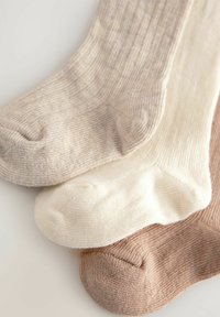 Drei Paar gerippte Socken in Beige, Creme und Hellbraun, aus weichem Material mit subtiler Textur und runden Zehen.