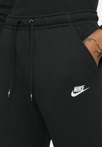 Mustat collegehousut pehmeästä kankaasta, joissa on joustava vyötärönyöri, sivutaskut ja valkoinen Nike-logo reidessä.