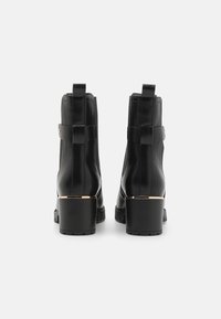 Stivali alla caviglia in pelle nera con finitura testurizzata, dotati di dettagli in tonalità oro e tacco a blocco. Linguette e silhouette elegante.