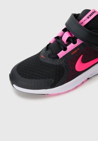 Chaussure de course Nike noire et rose avec un bout en maille, une sangle velcro et un logo Swoosh rose vif sur le côté avec le texte "Dynamic Fit".