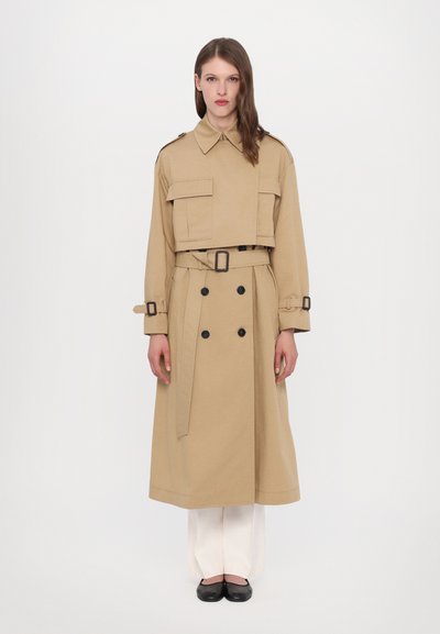 Beige trenchcoat met een ceintuur in de taille, dubbelzijdige knopen en grote klepzakken. Heeft een klassieke kraag en manchetbanden.