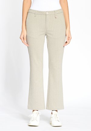 Beige ausgestellte Hosen aus strukturiertem Stoff, mit einem Knopfverschluss und Taschen, kombiniert mit weißen Sneakers.