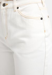 Λευκά τζιν από denim με αντίθετη κίτρινη ραφή, μεταλλικά κουμπιά και λεία υφή. Διαθέτουν μπροστινές τσέπες και εφαρμοστό σχεδιασμό.