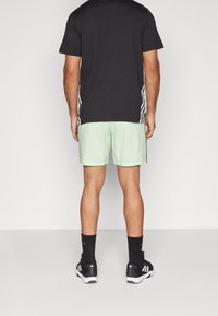 Svart kortärmad t-shirt, mintgröna shorts, svarta sportstrumpor och svarta löparskor med vita accenter. Minimalistisk design övergripande.