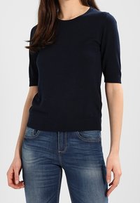 Suéter de manga corta azul marino con cuello redondo, dobladillo acanalado y textura lisa, combinado con jeans azules que presentan bolsillos estándar y costuras.