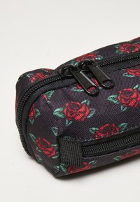 Black zippered pencil case with red rose pattern and green leaves. Features dual zipper pulls and textured fabric. Compact rectangular shape.