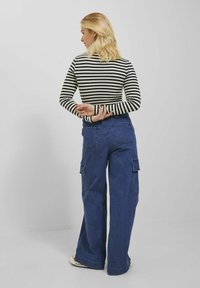 Mustriga pikkade varrukatega särk mustas ja valges, kombineeritud laia säärega siniste denim cargo pükste jaotistega, millel on mitu taskut ja kõrge vöökoht.