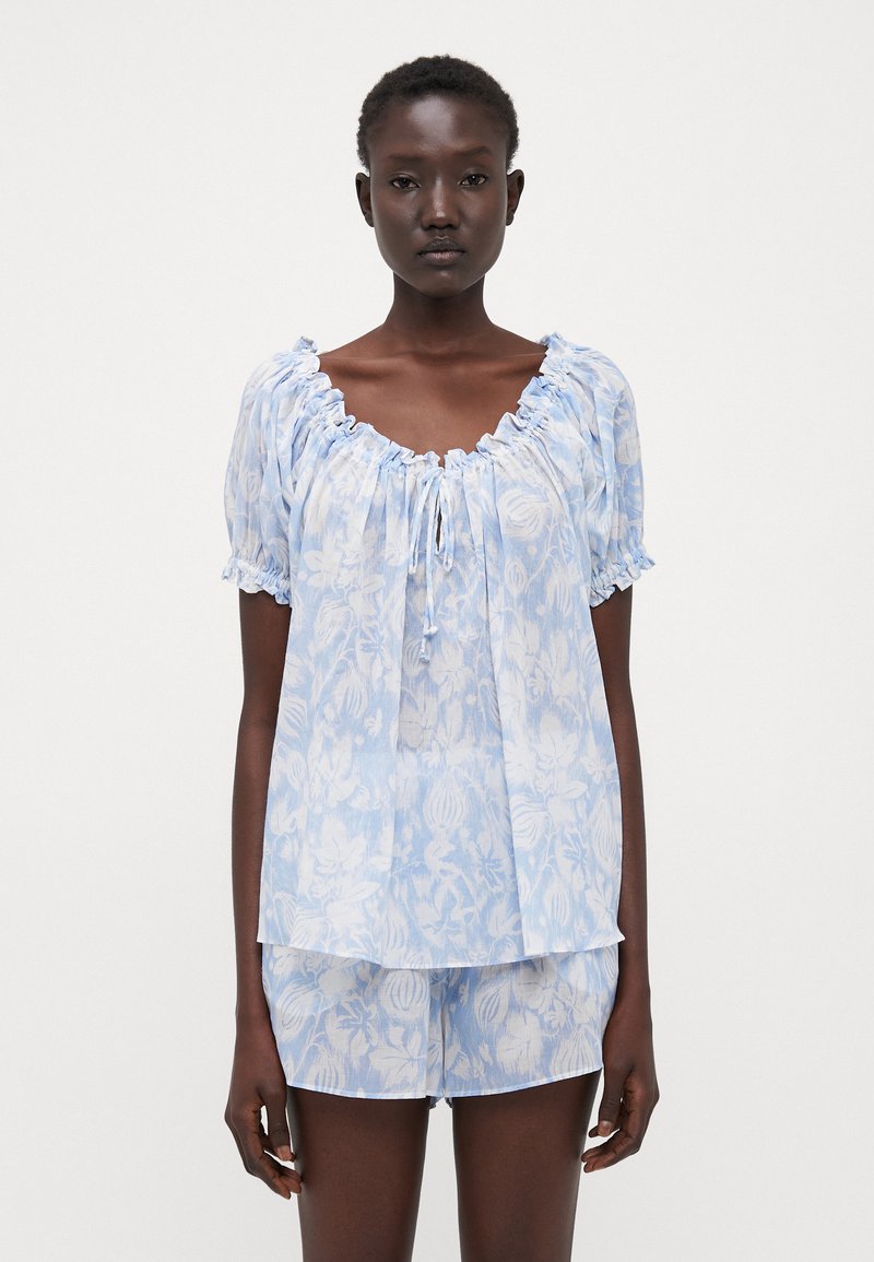 Light blue floral print top with ruffled neckline and short sleeves, paired with matching shorts. Flowing fabric with subtle pattern details.