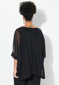 Top in tessuto nero trasparente con maniche ampie, vestibilità comoda e schiena solida. Presenta un orlo asimmetrico e accenti a motivo discreto sulle maniche.