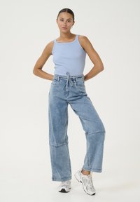 Gaiši zila ribota bez piedurknēm topa un brīvi pieguļošu, izbalējušu zilu denimu biksēm ar auklu viduklī. Modelis valkā baltas kedas. Kopumā gluda tekstūra.