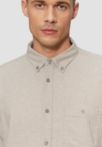 Lichtbeige overhemd met knopen en een textuurafwerking, voorzien van een puntige kraag, zes knopen en een klein borstzakje.
