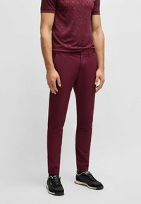 Bordowe spodnie slim fit o gładkiej fakturze, w zestawieniu z dopasowaną, wzorzystą bluzką z krótkim rękawem oraz czarnymi butami sportowymi z białymi akcentami.