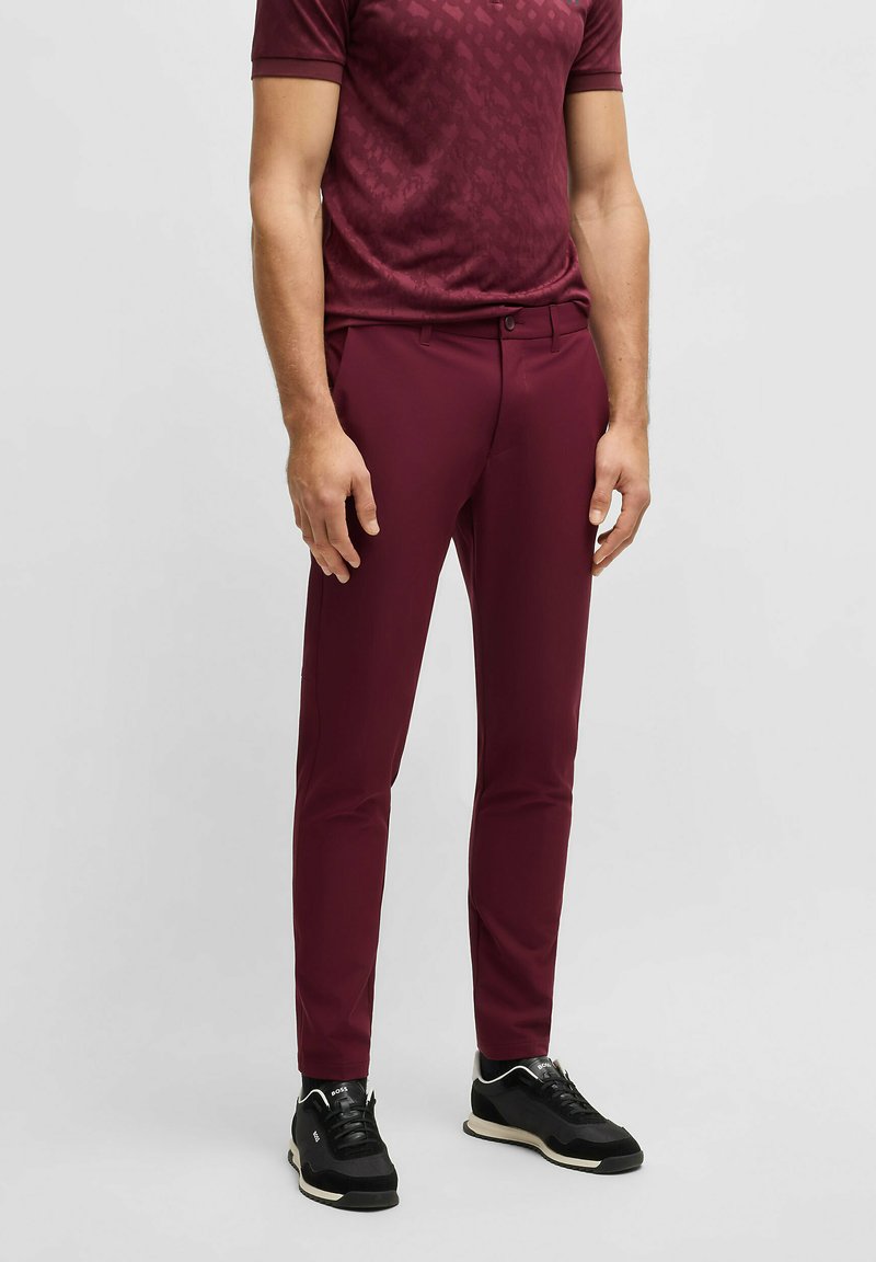 Bordowe spodnie slim fit o gładkiej fakturze, w zestawieniu z dopasowaną, wzorzystą bluzką z krótkim rękawem oraz czarnymi butami sportowymi z białymi akcentami.