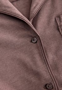 Chemise boutonnée marron en tissu doux et texturé. Dotée d'un col, de boutons sur le devant et d'une poche poitrine pour un design pratique.