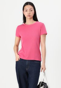 T-shirt rose côtelé à manches courtes et col rond, associé à un jean bleu foncé et un sac à main blanc. Design épuré, sans motifs.