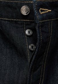 Pantalones vaqueros de denim con tela azul oscuro, botones de metal plateado y costuras en oro contrastante a lo largo de las costuras y los bolsillos.