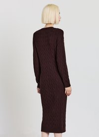 Robe longue bordeaux en tricot avec un motif torsadé, manches longues et poignets côtelés. Le modèle est ajusté et arrive mi-mollet.