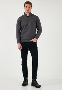 Pullover grigio a mezza zip con maniche lunghe, in misto cotone, vestibilità strutturata, abbinato a jeans scuri e stivali neri con lacci.