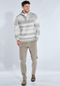 Grau-weiß gestreifter Pullover mit halbem Reißverschlusskragen, kombiniert mit beigen Cordhosen und braunen Wildlederstiefeln.