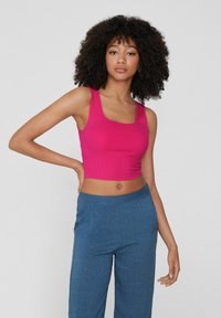 Top corto aderente a coste di un vivace colore rosa, con spalline larghe e scollatura quadrata, abbinato a pantaloni blu larghi e strutturati.