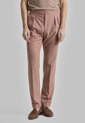 Pantalones plisados color rosa en una tela texturizada. Con una cinturilla alta y dobladillos rematados. Combinados con mocasines de ante marrón.