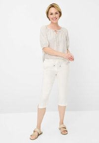 Chemisier léger à rayures avec un col à nouer, associé à un pantalon blanc court avec une taille élastique et des fentes sur les côtés. Sandales beiges.