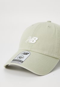 Light beige baseball cap with white embroidered "NB" logo on front and a sticker on the brim reading "'47 Clean Up Adjustable."