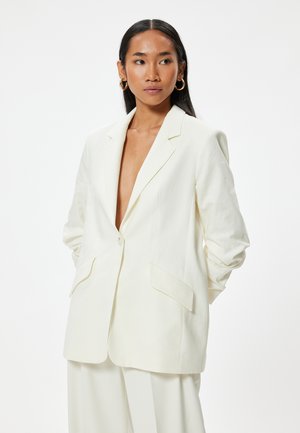 White linen blazer with a notch lapel, single button closure, and two front pockets. Features a relaxed fit and slightly oversized design.