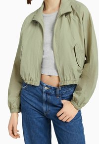 Light green cropped jacket with a textured finish, two side pockets, and elastic cuffs. Paired with high-waisted blue denim jeans.