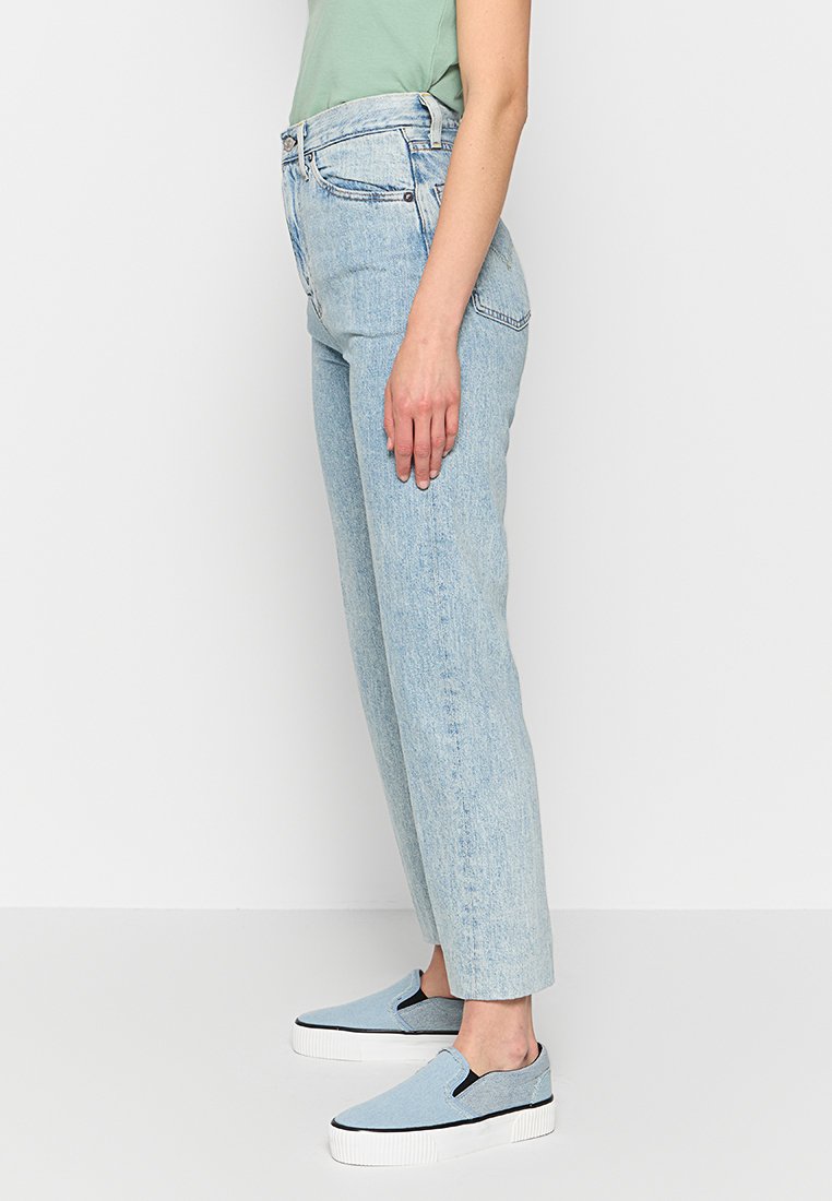 Jean taille haute bleu clair avec une coupe droite. Fabriqué en denim, avec des coutures minimales et des poches latérales. Associé à des chaussures slip-on bleu clair.