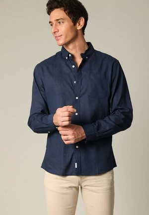 Chemise boutonnée bleu marine avec une poche poitrine, fabriquée dans un tissu texturé. Dispose de manches longues et d'un col classique.