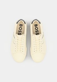 Cream-colored sneakers with lace-up closure, rubber soles, and a black accent at the heel. “BOSS” logo printed on the insole. Flat design.