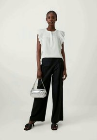 Fehér, rövid ujjú blúz, fodros részletekkel, széles fekete nadrággal párosítva. Ezüst színű kézitáska lánc részletekkel. Fekete, nyitott orrú cipők.