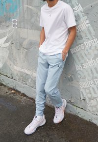 Vit t-shirt med kort ärm och svart Jordan-logotyp, ljusblå joggingbyxor med svart Jordan-logotyp, och vita sneakers med pastellfärger.