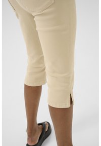 Beige housut, jotka on lyhennetty ja slim fit -malliset, joissa on sivuaukot helmassa ja sileä pinta. Yhdistetty mustiin tasapohjaisiin sandaaleihin.