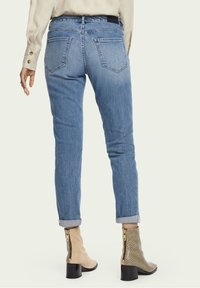 Jeans de mezclilla azul claro con corte recto y bolsillos traseros, combinados con botines beige con estampado de serpiente y cremalleras laterales.