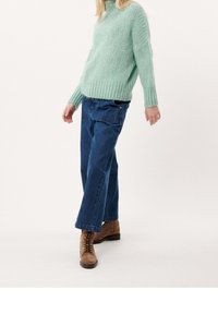 Mintgrön, tjockstickad tröja med ribbade manschetter. Lösa, blå denim cargo-byxor och bruna snörkängor. Enkel, texturerad outfit.