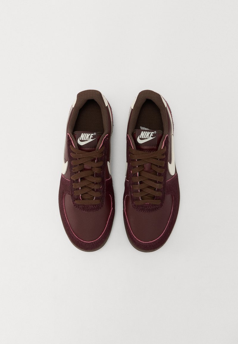 Baskets Nike bourgogne avec un design lisse et texturé, ornées de lacets marron, d'un logo blanc et d'accents roses le long de la semelle.