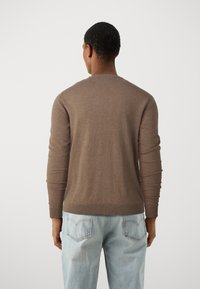 Brun stickad tröja med långa ärmar, rundad halsringning och ribbad fåll, i kombination med ljusblå, löst sittande jeans med hjärtformade fickor.