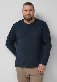 Marineblaues Langarm-T-Shirt aus Baumwollmischung. Mit rundem Ausschnitt, lockerem Schnitt und weicher Textur. Kombiniert mit hellbraunen Hosen.