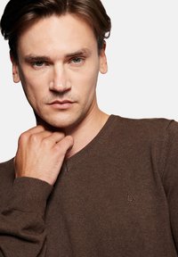 Brązowy sweter dzianinowy z dekoltem w szpic, teksturowana tkanina i subtelne haftowane logo na lewej piersi.