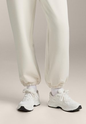 Witte sportieve sneakers van textuurmesh en leer, met zwarte accenten, ronde neuzen en verstelbare veters. Gecombineerd met crèmekleurige taps toelopende joggers.