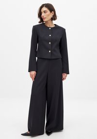 Black tailored suit with a cropped blazer, gold buttons, and wide-leg pants. Smooth texture and clean lines, showcasing a minimalist design.