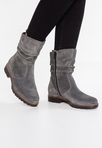 Bottines en suède gris avec des revers souples, fermeture éclair sur le côté et semelles en caoutchouc texturé. Le design présente des coutures subtiles et une forme de bout arrondi.