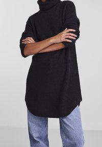 Svart polotröja med ribbad textur, ärmar i medellängd och en avslappnad passform, ihop med ljusblå denimjeans.