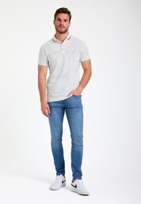 Polo shirt grigio chiaro con motivi sottili, maniche corte, dettagli del colletto neri, abbinato a jeans blu slim-fit e sneakers bianche.