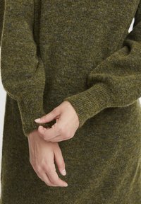 Abito lavorato a maglia in lana verde oliva scuro con una finitura testurizzata, caratterizzato da maniche a sbuffo e polsini a costine, che enfatizza comfort e calore.