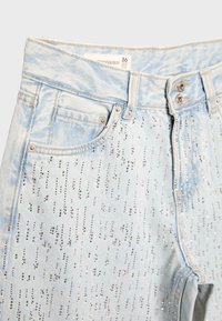 Světlé modré džíny z denimu se stříbrnými ozdobami z kamínků, přední kapsy, dvojité zapínání na knoflíky a viditelná štítek s velikostí 36.