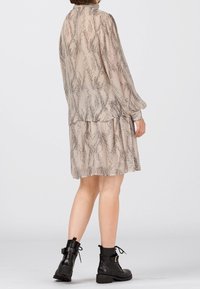 Abito beige a fantasia con maniche lunghe e gonna a strati; realizzato in tessuto leggero con disegni astratti neri; abbinato a stivaletti neri alla caviglia.