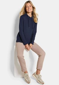 Pullover blu navy con cappuccio, maniche lunghe e cordini. Abbinato a pantaloni beige chiaro e sneakers avorio. Tessuto di qualità liscia.